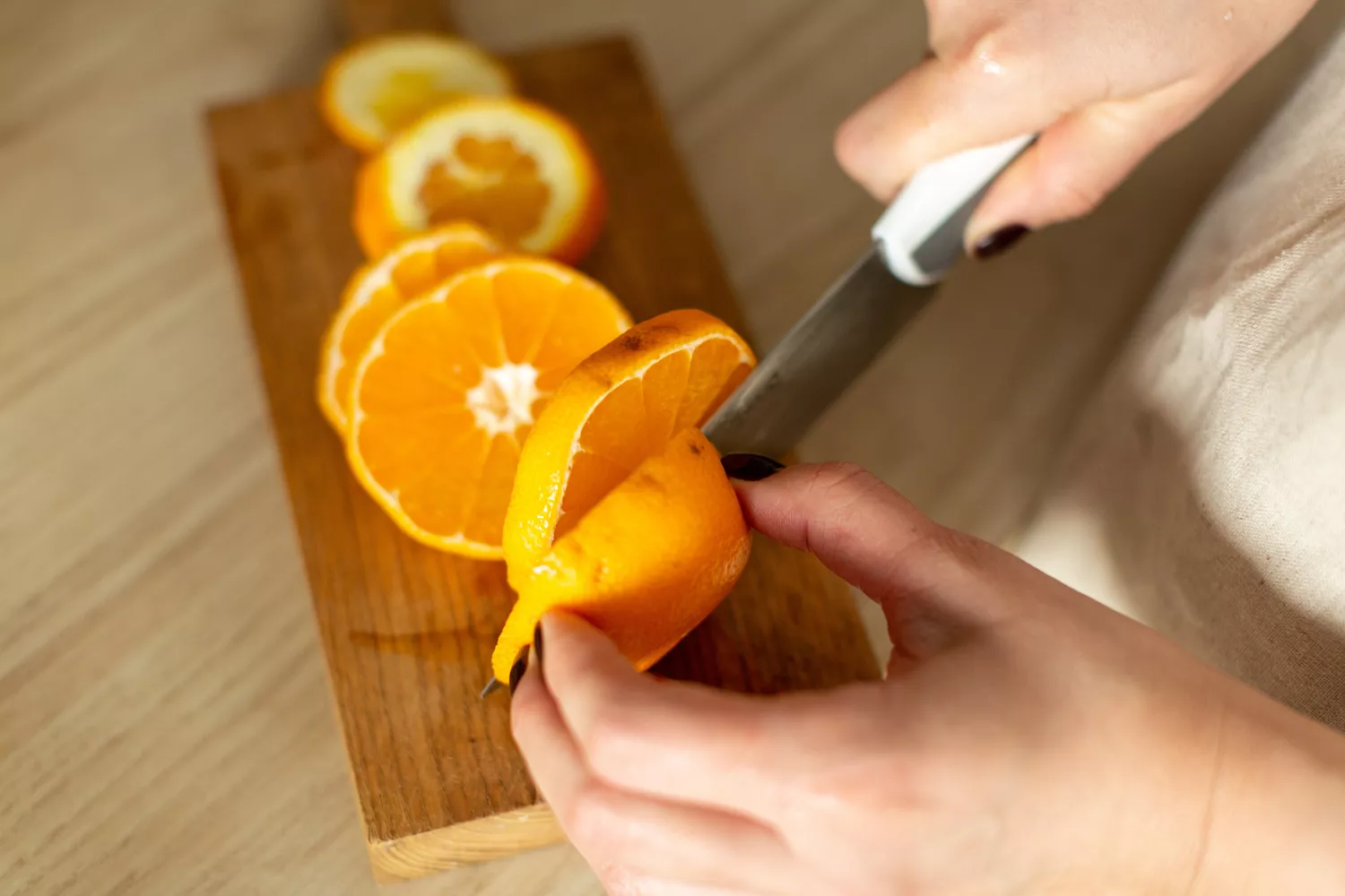 A woman slicing an orange on a wooden board in a bright kitchen environment.
