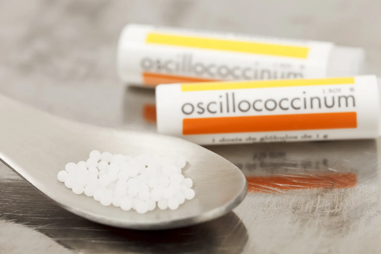 Macro view of homeopathic globules and Oscillococcinum dispenser tubes.