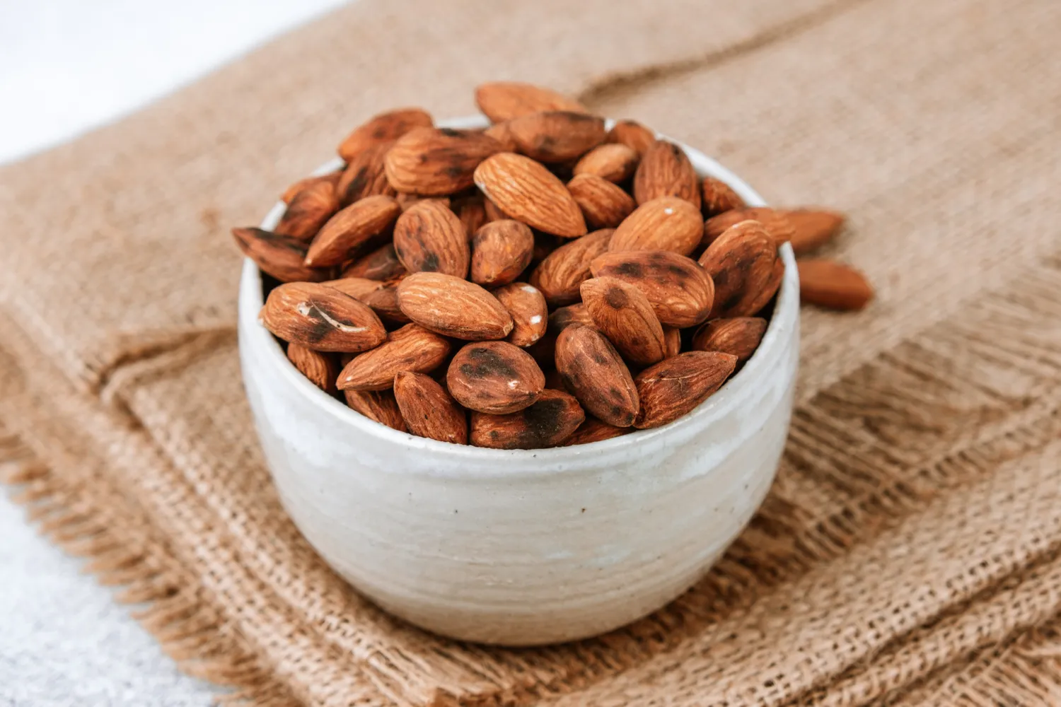 Close-up of a wooden bowl filled with roasted almonds.