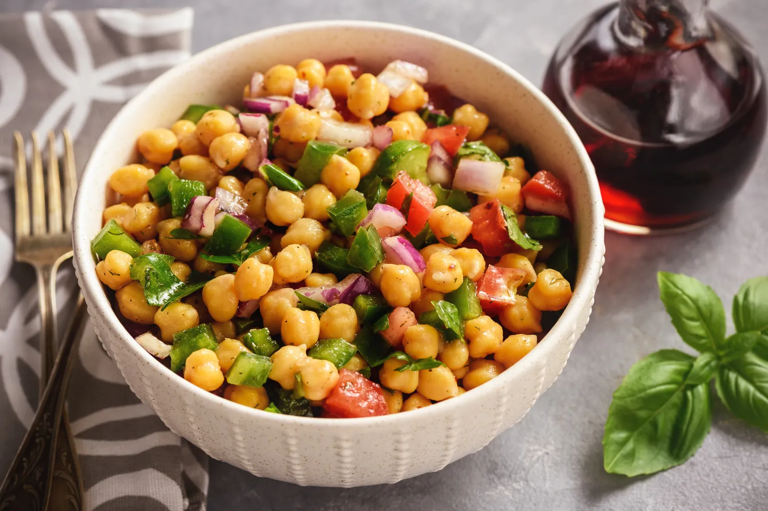 A bowl of chickpea salad with tomatoes, greens, and dressing.