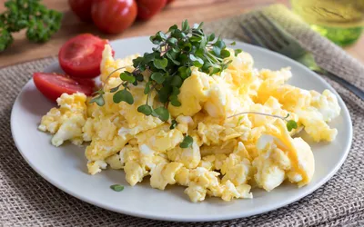A plate of scrambled eggs garnished with greens and served with fresh tomatoes.