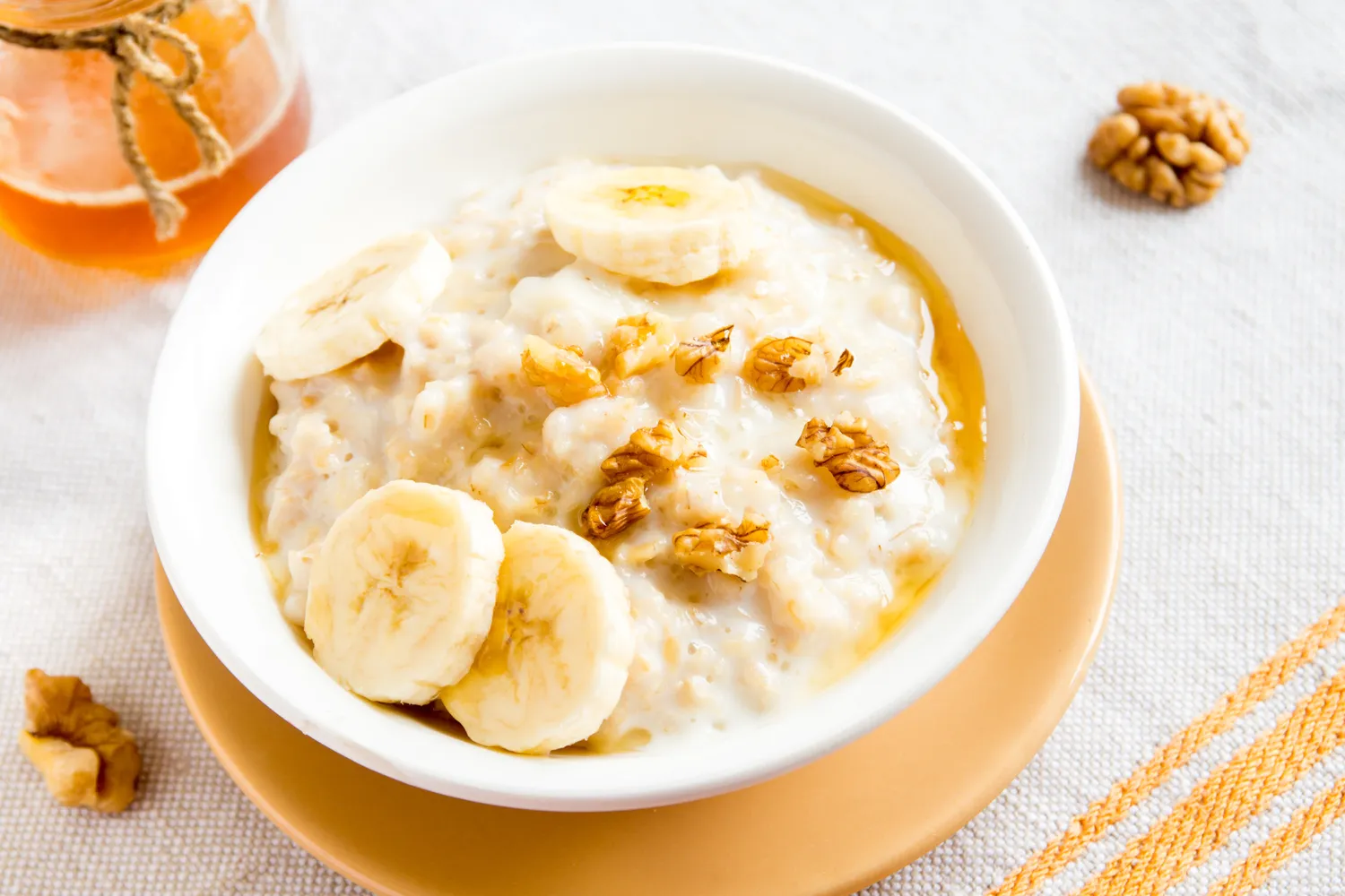 Bowl of oatmeal topped with banana slices and walnuts.
