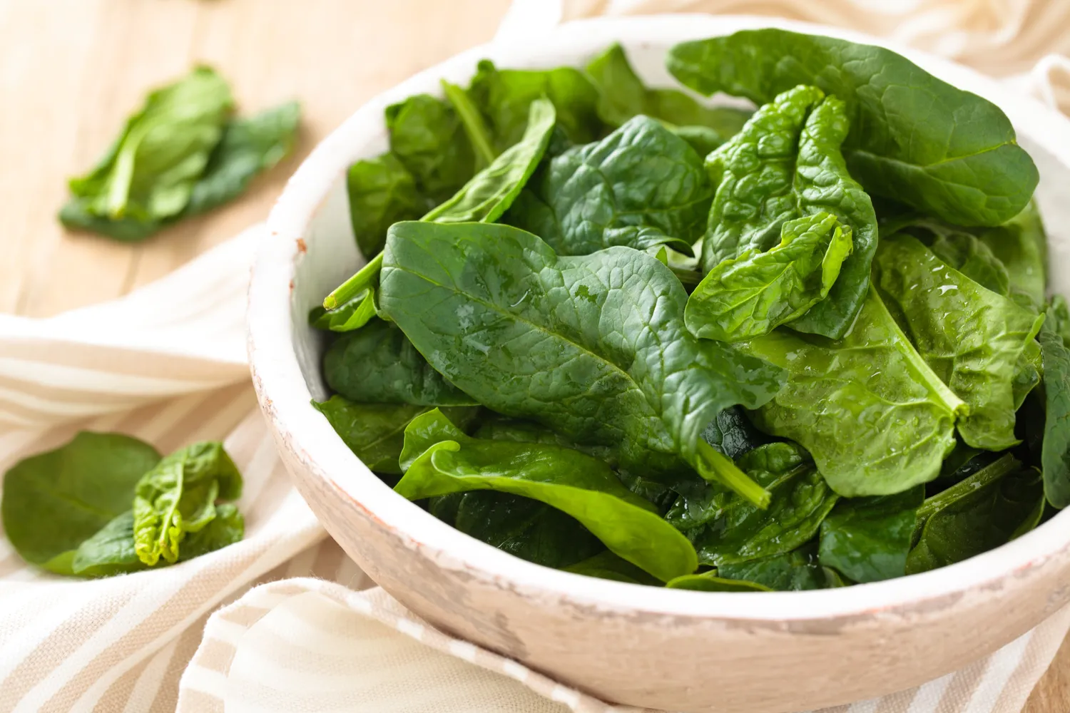 Fresh green spinach leaves in a bowl on a striped kitchen towel.