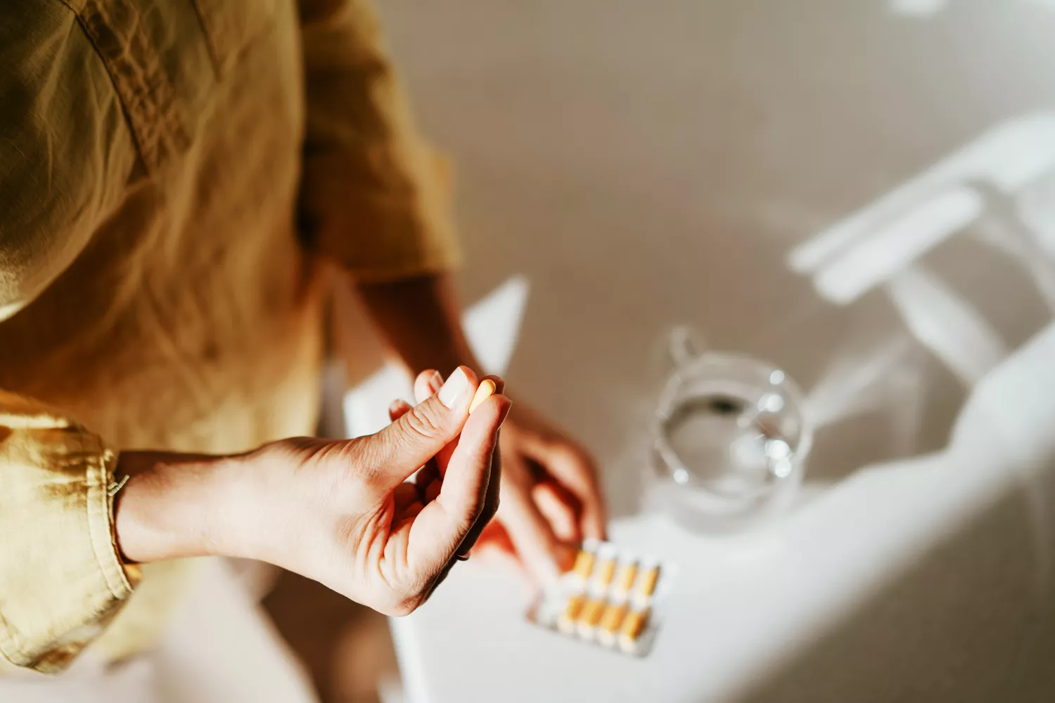 A close-up of a person holding a clear probiotic supplement capsule between their fingers.