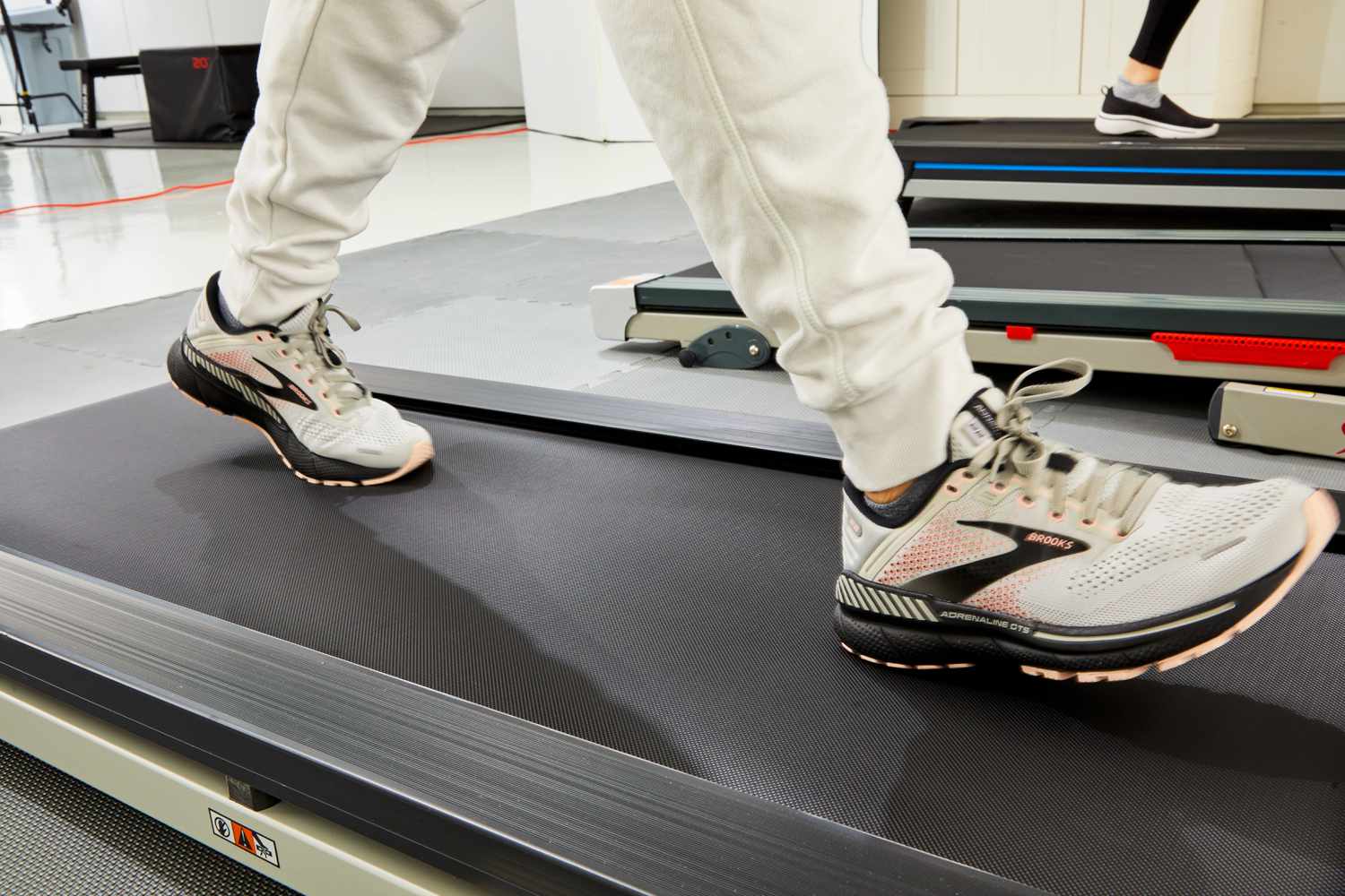 A person wearing Brooks stability running shoes performing a gait analysis on a treadmill in a lab setting.