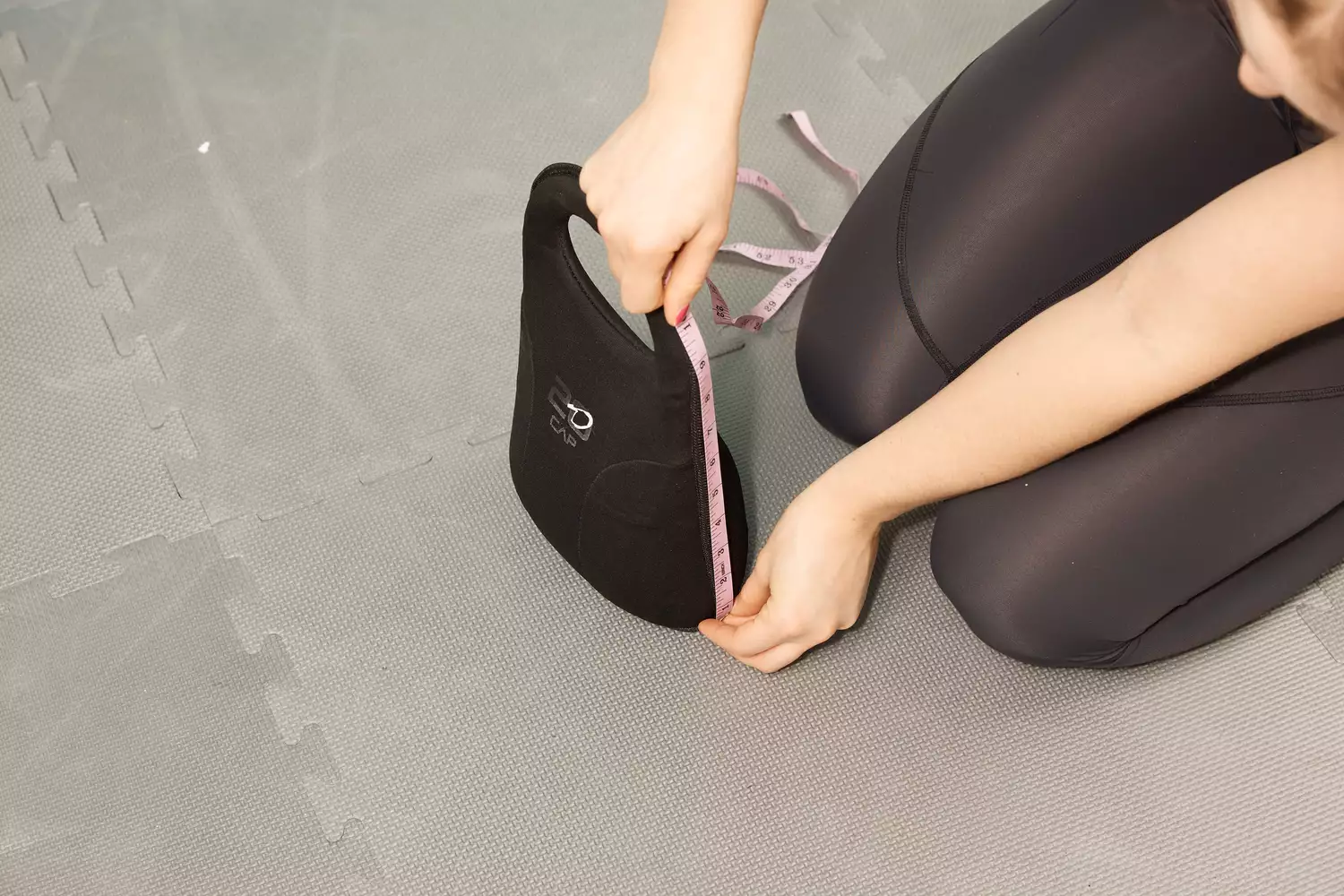 A person using a measuring tape to check the dimensions of a soft kettlebell on a gym mat.