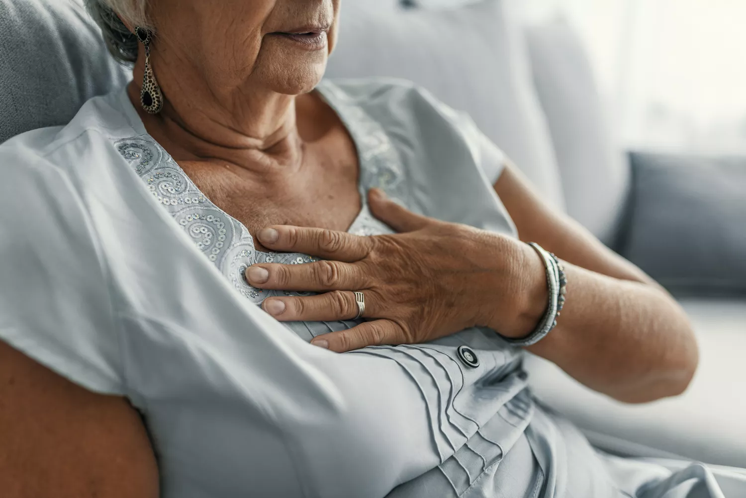 A woman clutching her chest while sitting indoors, suggesting persistent cardiac or esophageal discomfort.