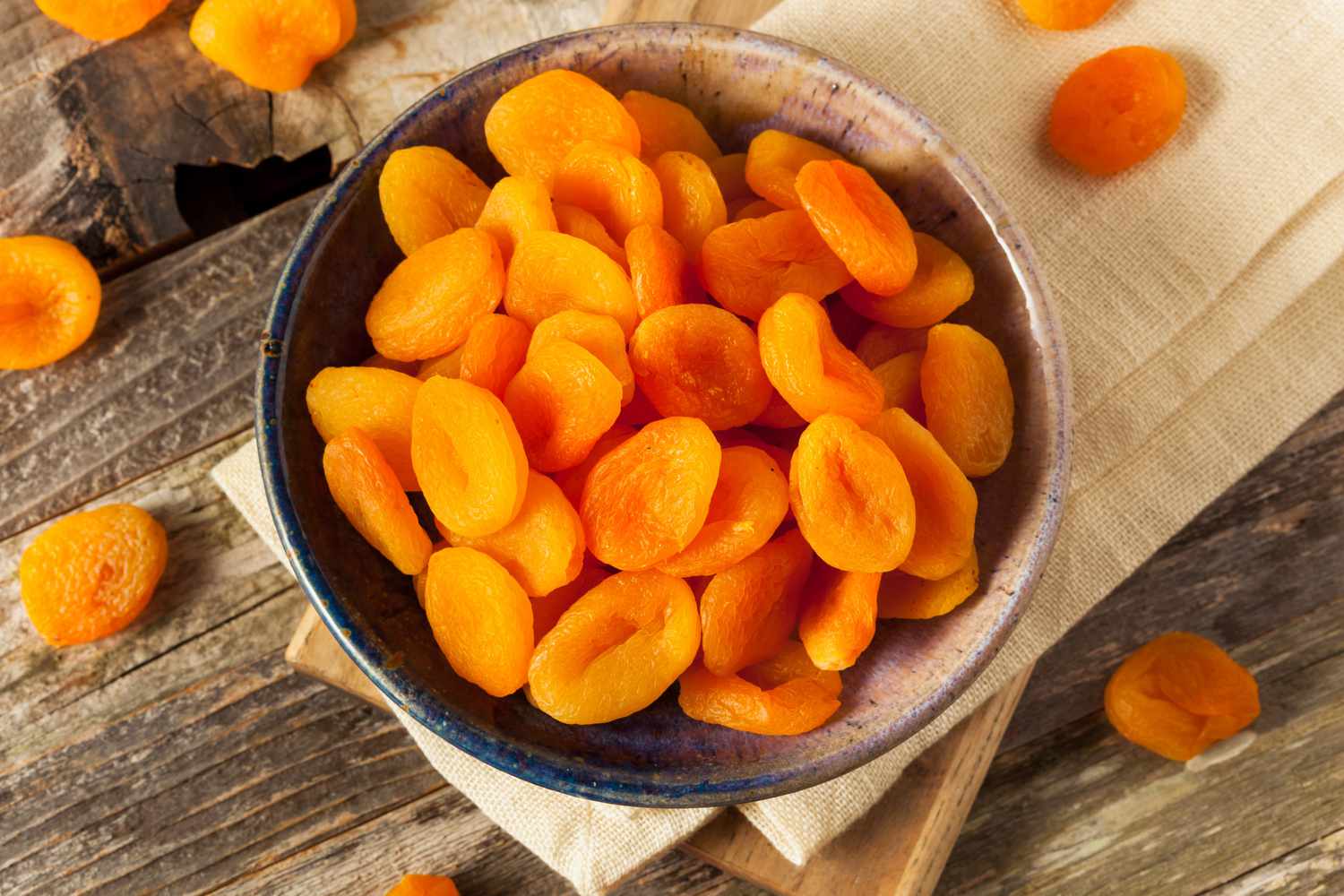 A small wooden bowl filled with orange dried apricots on a neutral background.
