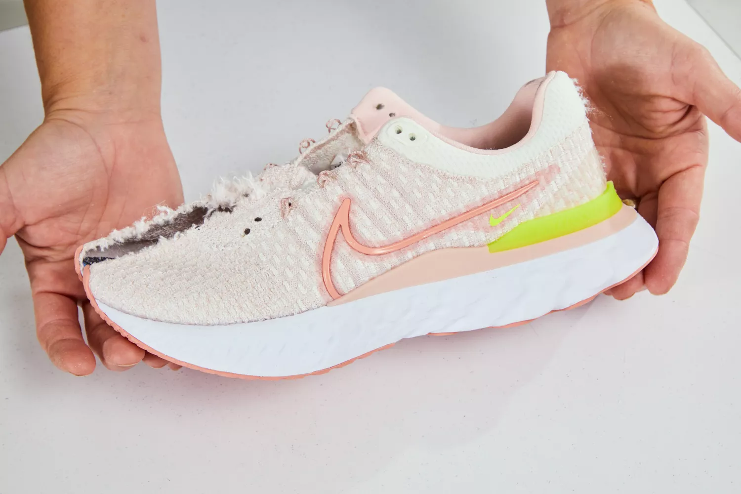 Hands holding a worn-out Nike React Infinity 3 shoe with visible tears and sole degradation.