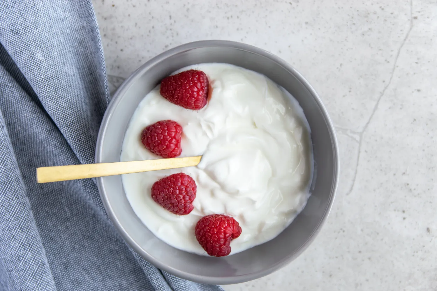 A bowl of yogurt with fresh raspberries and a wooden spoon.