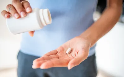 A person pouring a single white supplement pill from a bottle into their hand.