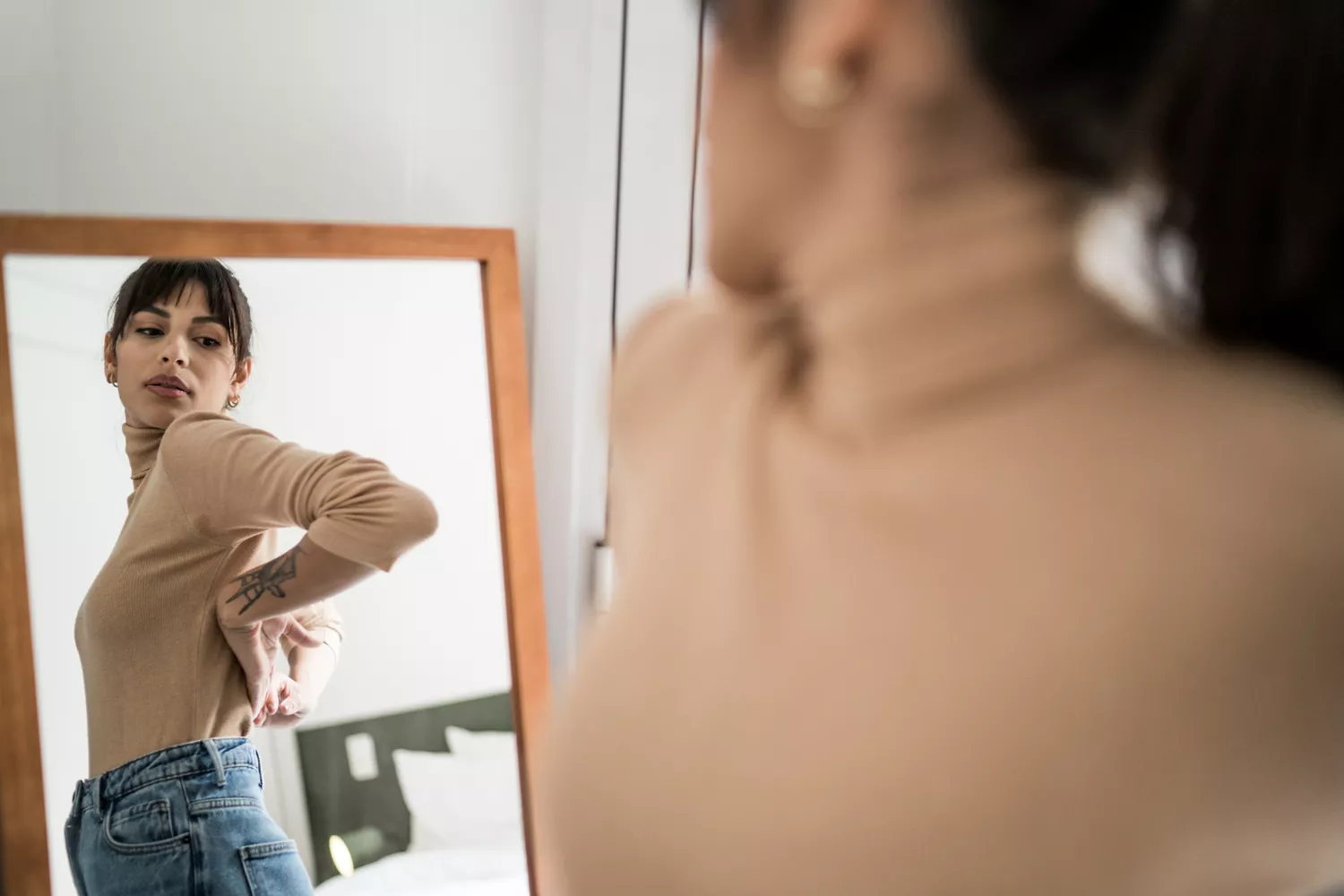 A person standing in front of a mirror looking concerned while observing their bloated midsection.