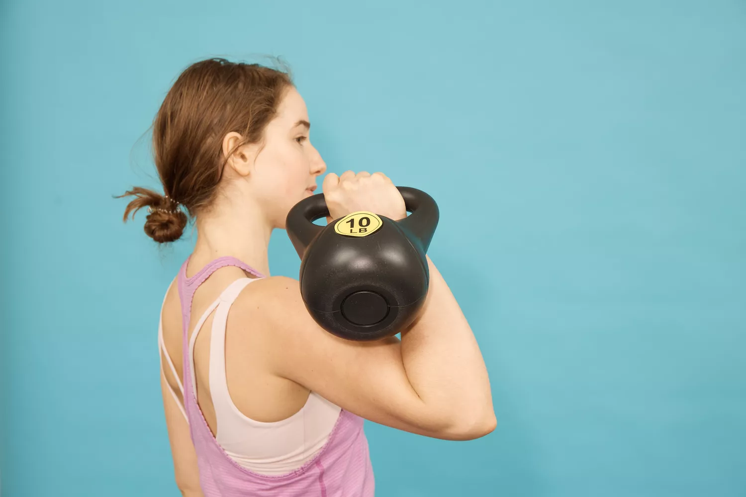 A woman in athletic wear performing an overhead press with a 10 LB kettlebell.