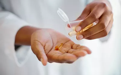 A close-up of a healthcare provider holding a supplement bottle and pouring a single capsule into their hand.