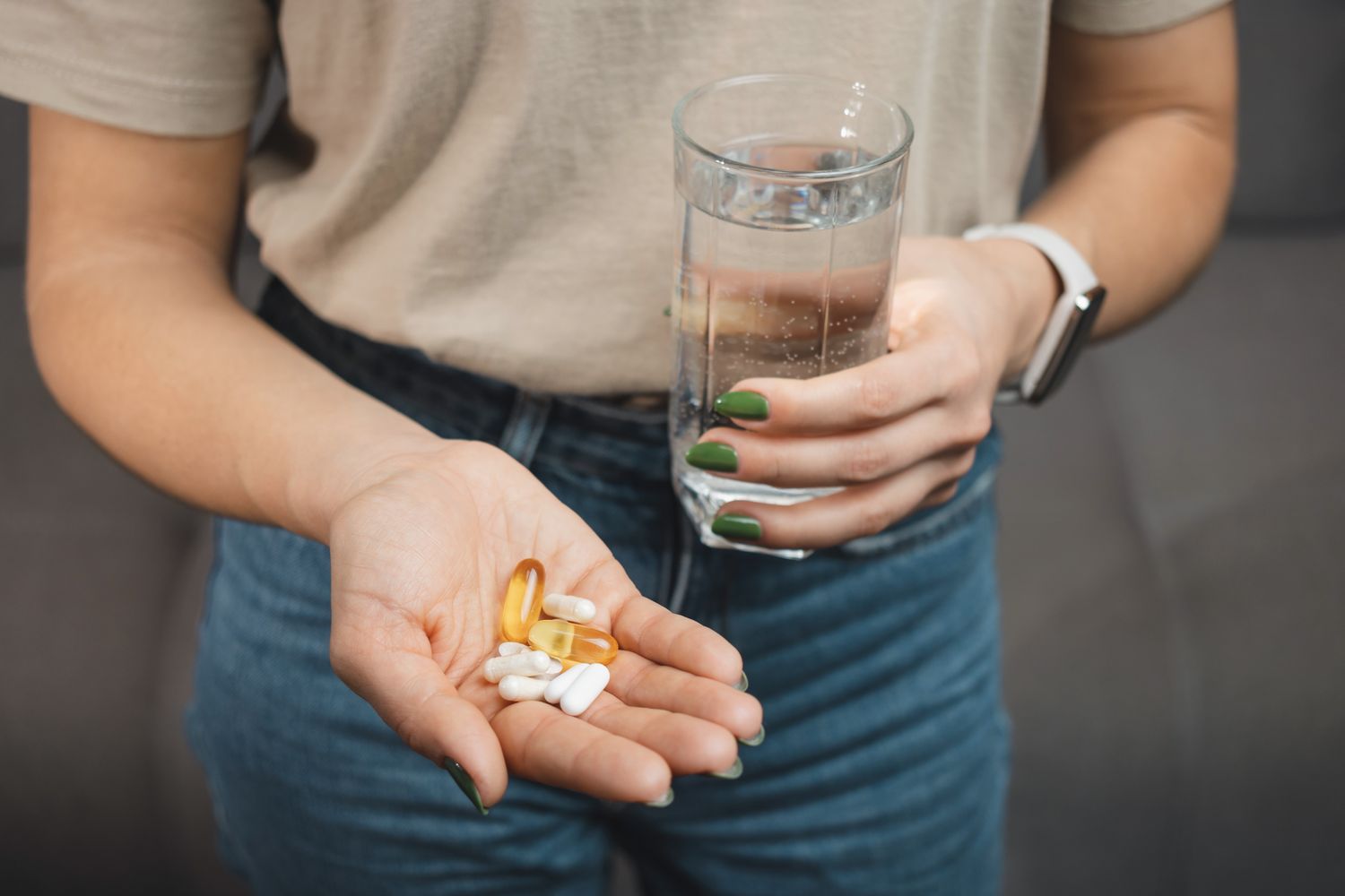 Close-up of a person holding fish oil supplements and white pills in their hand.