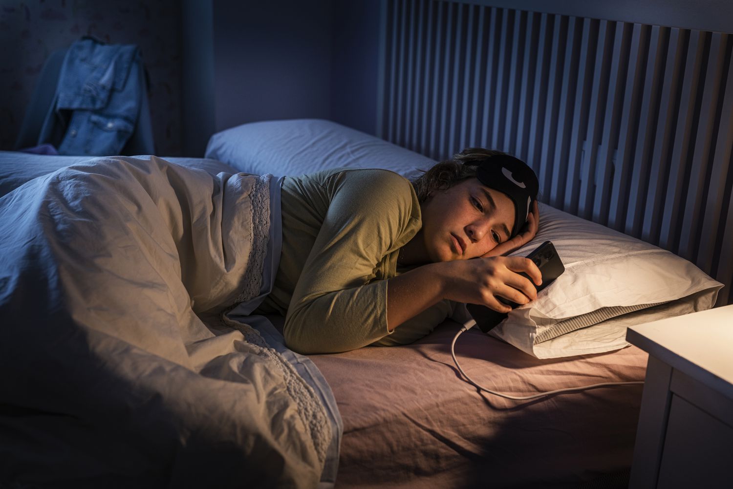A young person using a smartphone in a dimly lit room to complete a digital health assessment.