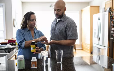 A man and a woman in a kitchen looking at supplement bottles, discussing health and nutrition.