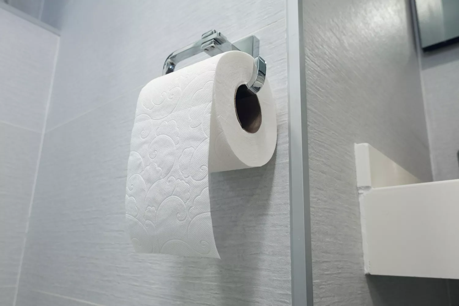 A close-up of a white toilet paper roll in a bathroom setting.