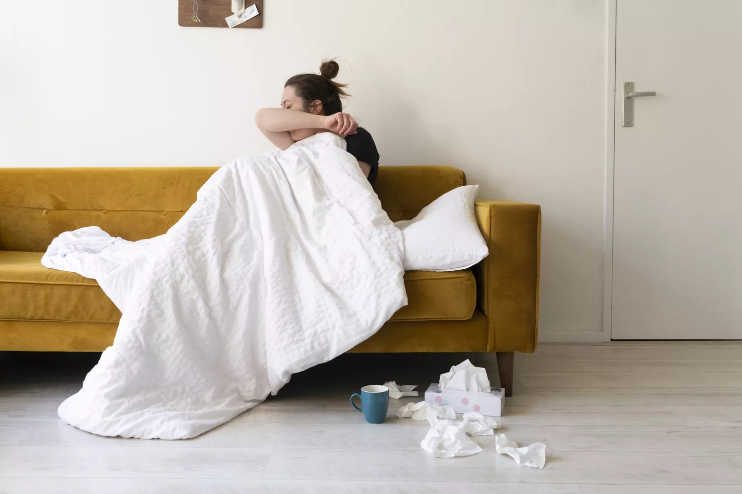 A sick woman wrapped in a blanket resting on a couch.