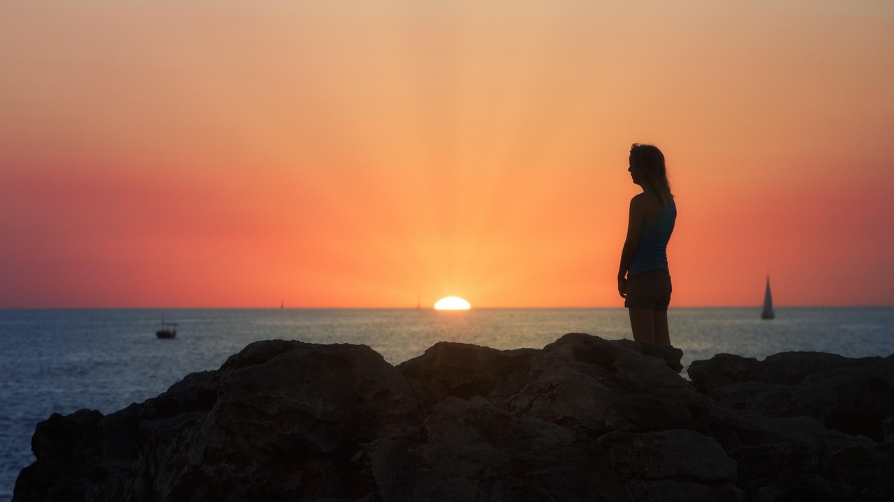 A person sitting in a peaceful meditation pose by the sea during sunset