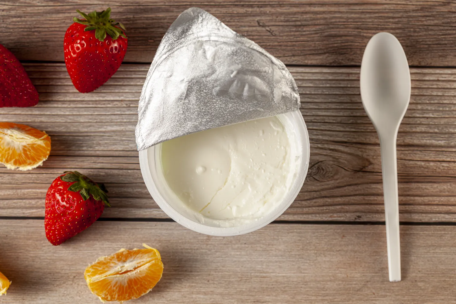A bowl of plain yogurt with fresh strawberries and orange slices.