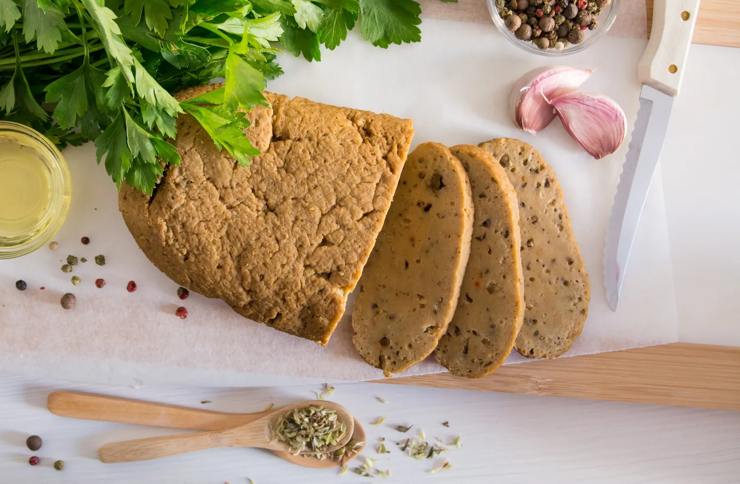 Sliced seitan on a cutting board with herbs, garlic, and spices.