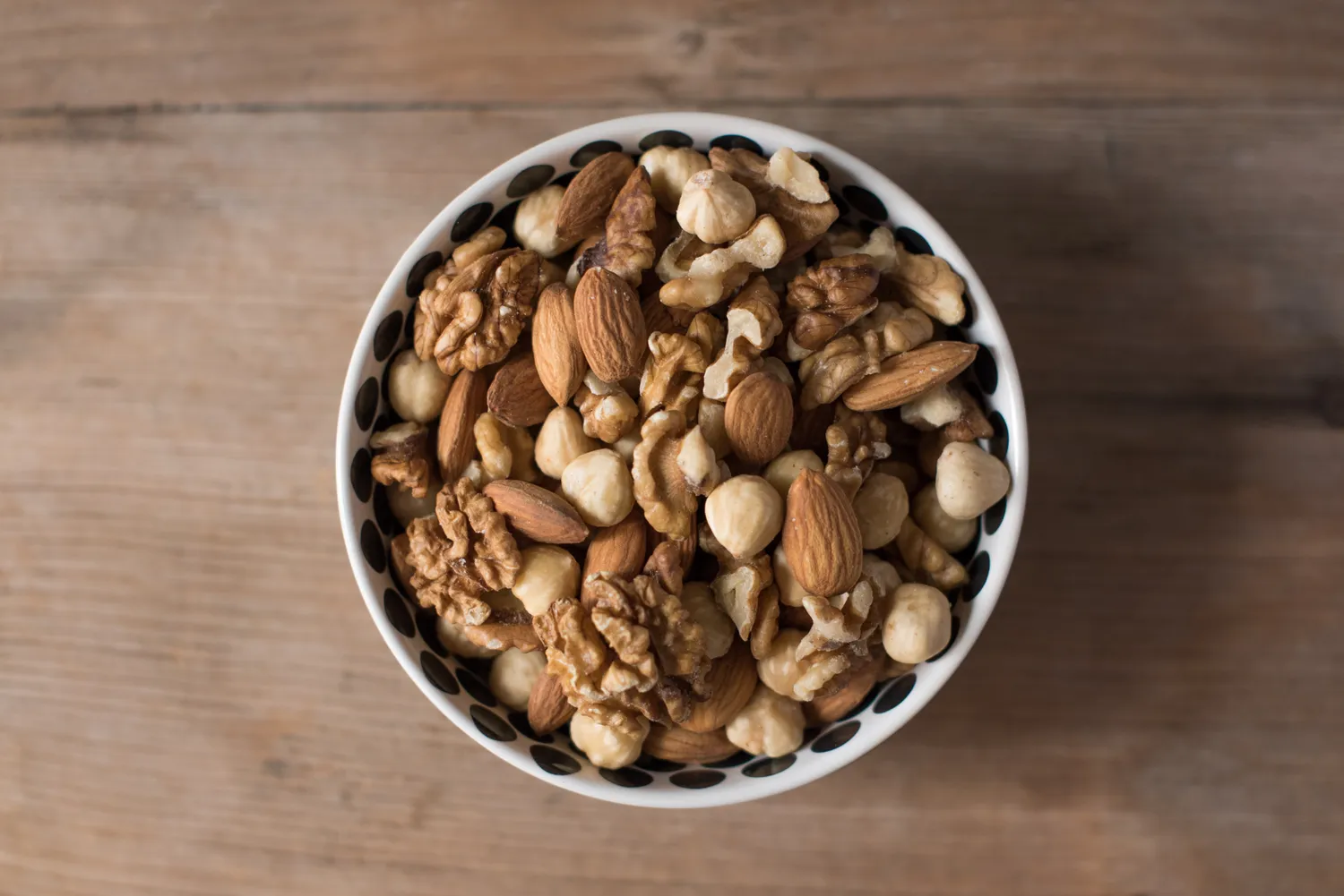 A variety of mixed nuts in a bowl on a wooden surface.