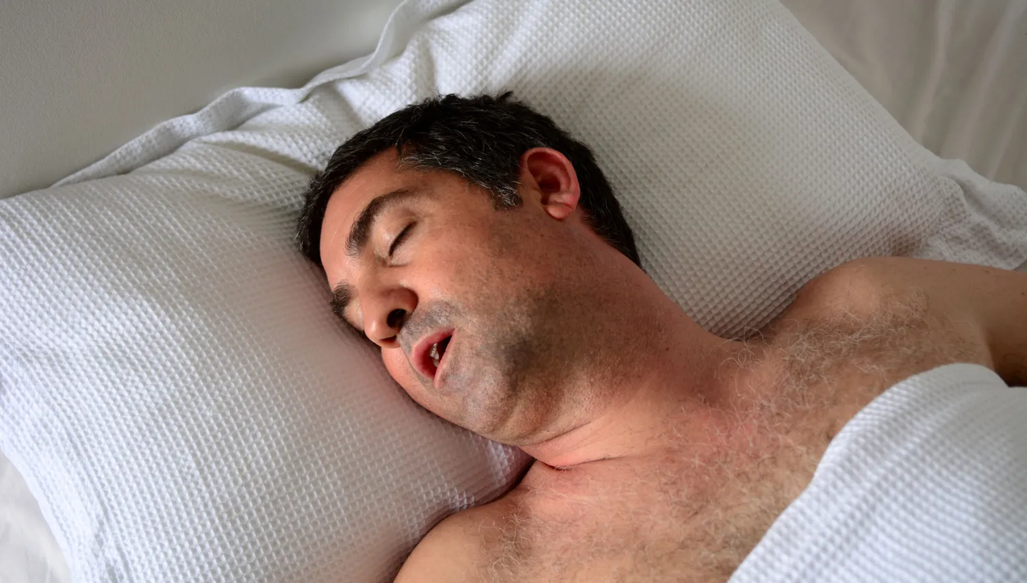 A person in bed snoring, highlighting the physical impact of obstructed breathing.