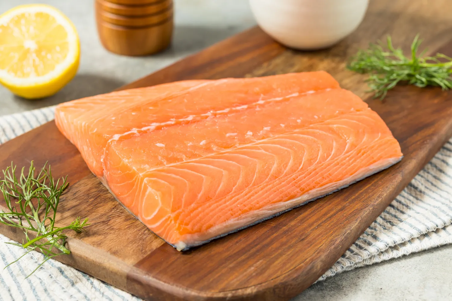 Raw salmon fillets on a wooden board with herbs and lemon.