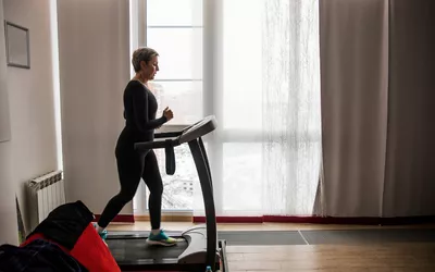 A woman running on a treadmill in a sunlit home interior.