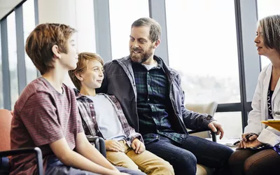 A female doctor sitting with a father and children in a medical office having a discussion.