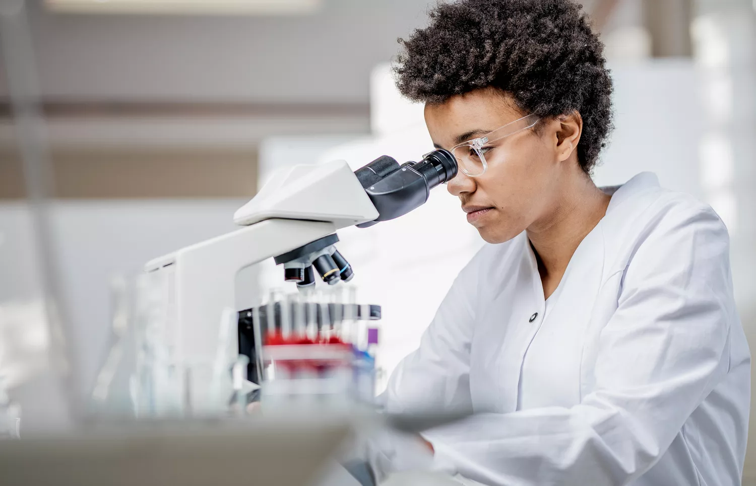 A scientist in a white lab coat using a microscope in a diagnostic laboratory.