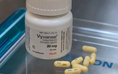 A pharmaceutical bottle of Vyvanse capsules spilled on a reflective surface, representing clinical ADHD medication.