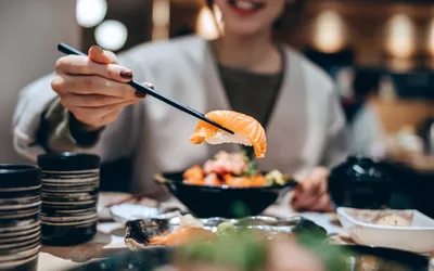 A woman eating fresh salmon sushi with chopsticks at a restaurant.