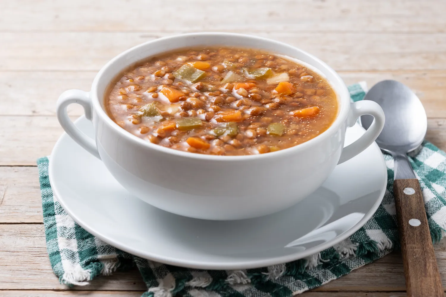 A warm bowl of lentil soup with vegetables on a rustic wooden table.