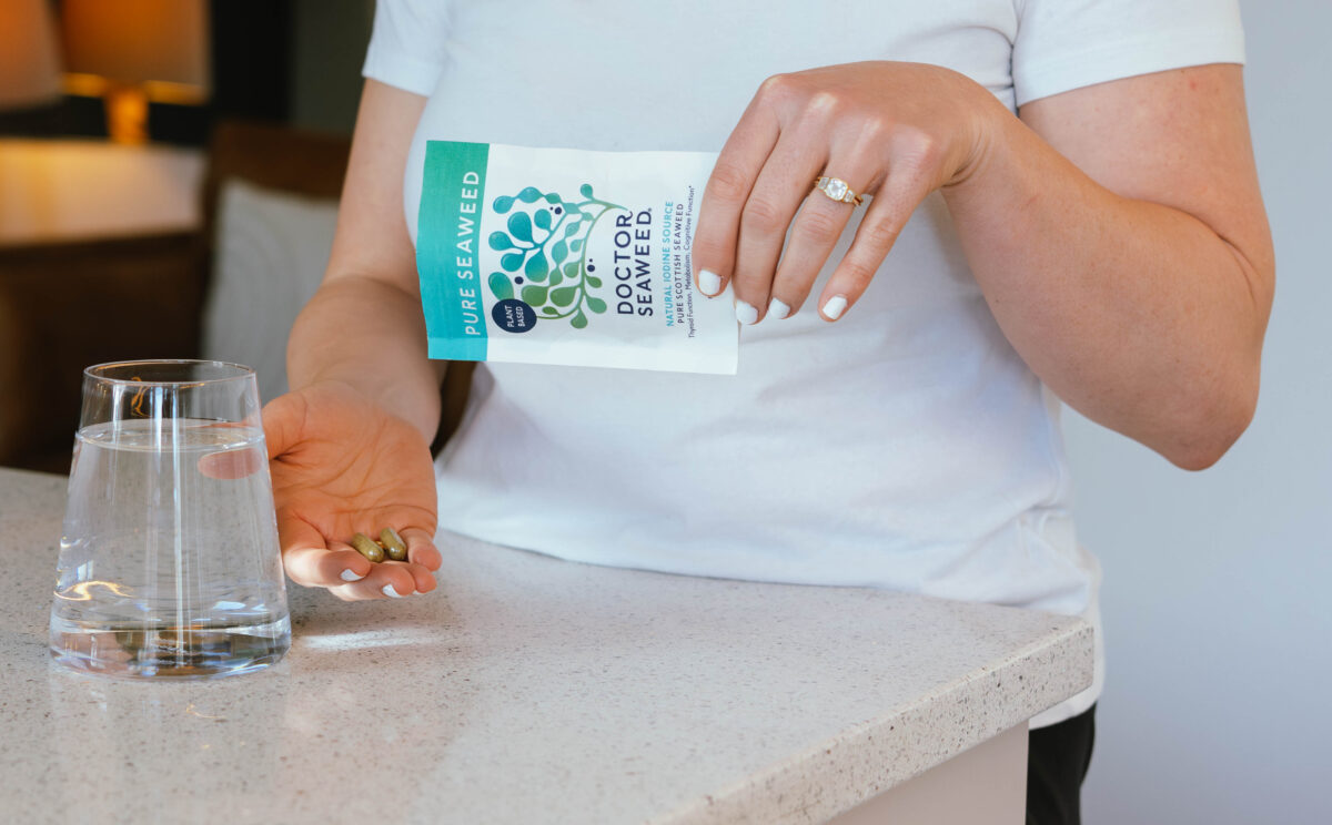 A person holding a bottle of seaweed supplements in a bright, modern kitchen.