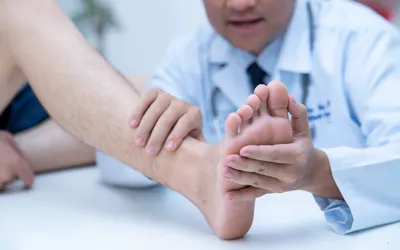 A medical professional in a clinical setting examining a patient's foot for signs of skin or joint issues.