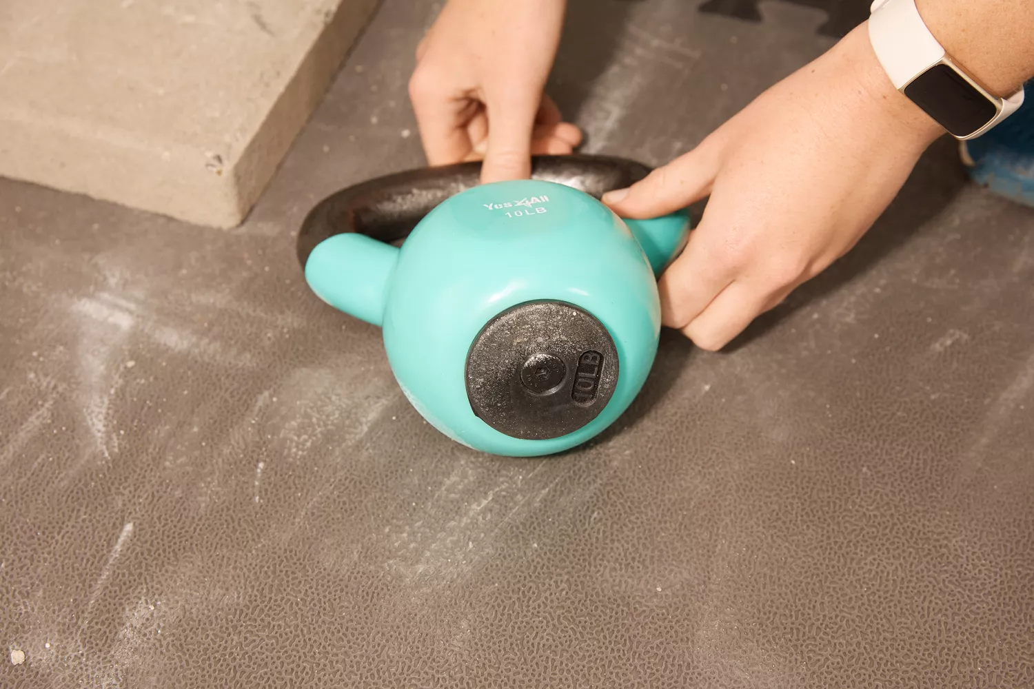 Close-up of hands gripping a turquoise 10LB vinyl-coated kettlebell handle.