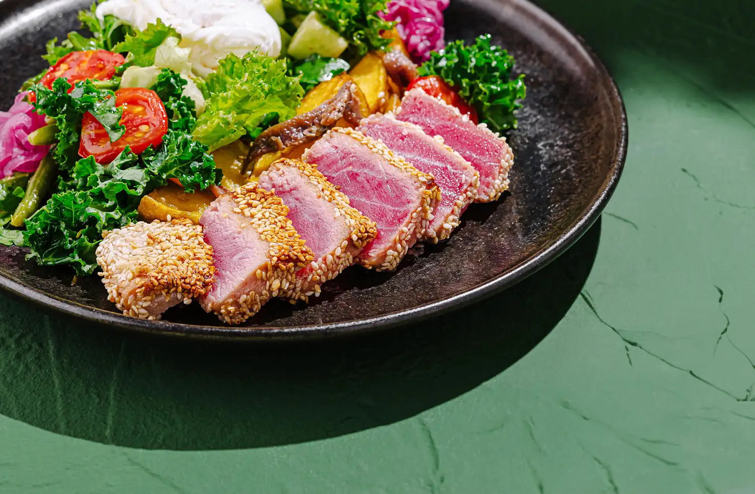 Slices of seared tuna with a sesame crust on a bed of mixed greens.