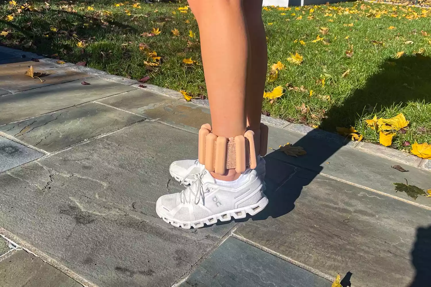 A person stands outdoors on a stone path wearing beige Bala Bangles over white running shoes.