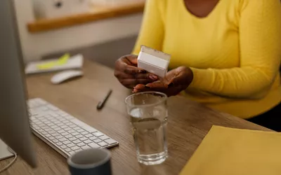 A person at an office desk holding a pill organizer next to a glass of water, focusing on wellness routines.